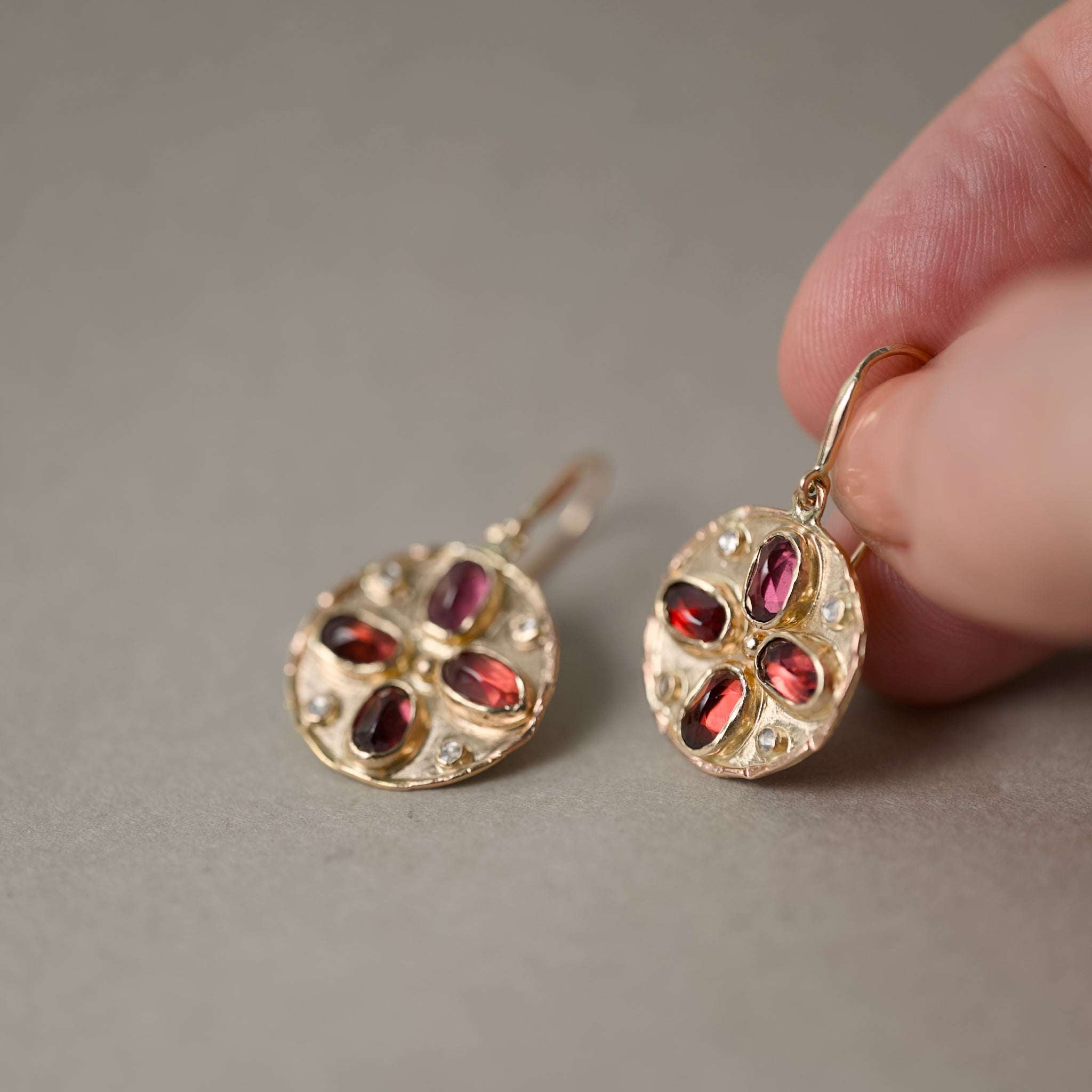 Florin alta garnet gold earrings held in fingers