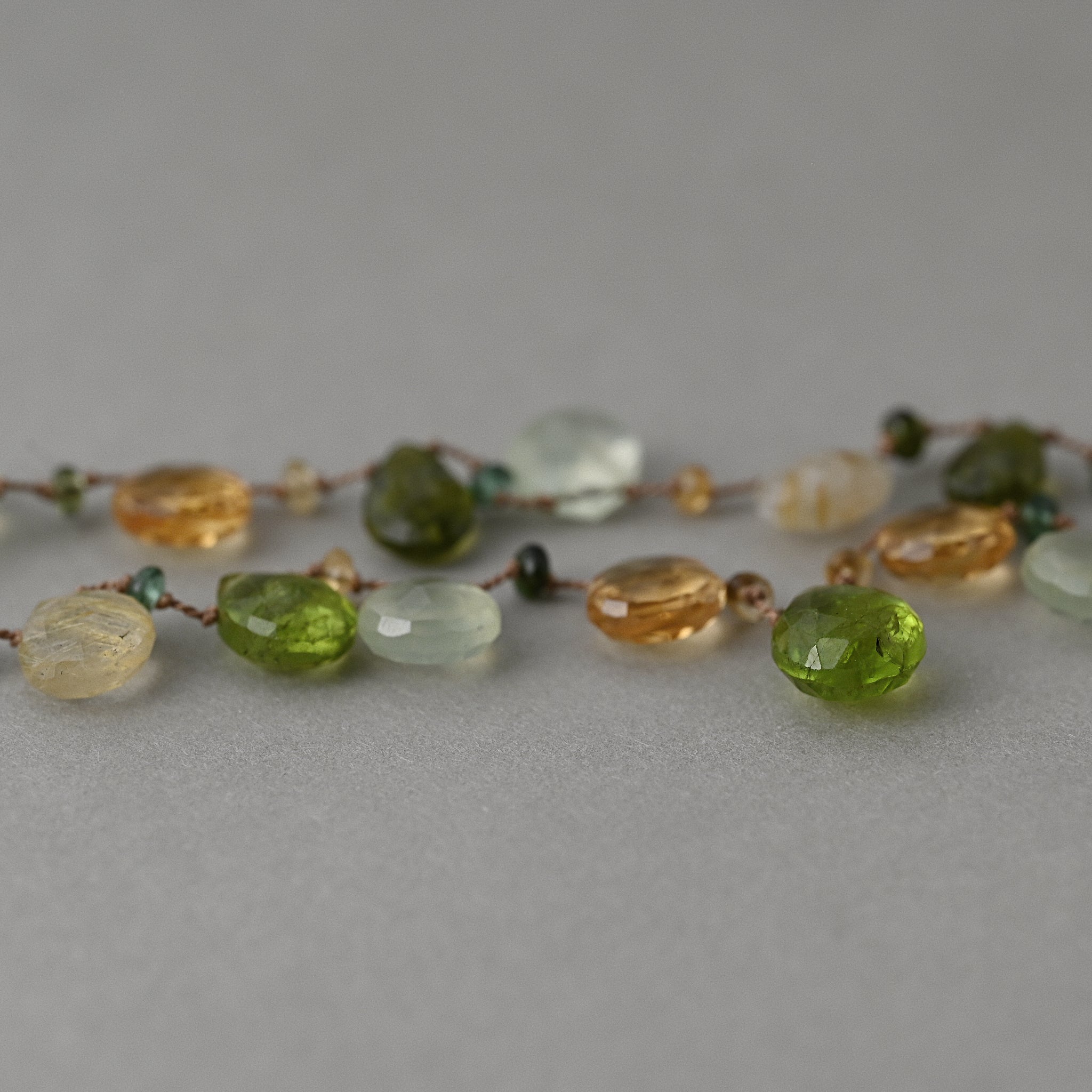 A close up of Lido silk necklace knotted with peridot, citrine, prehnite, quartz gemstones and finished with a 14ct gold clasp