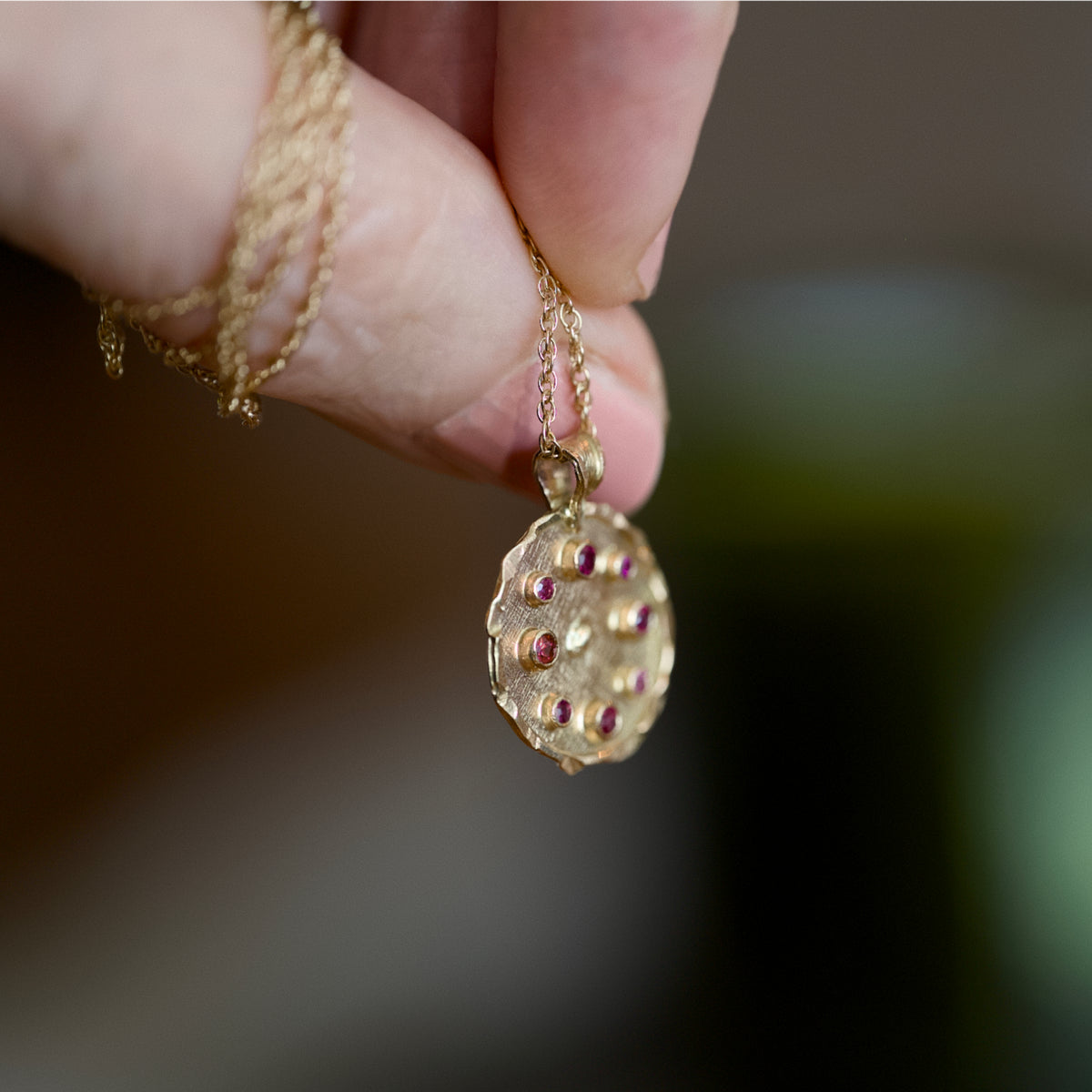 Hand holding a Florin ruby medallion necklace in solid 14ct gold by Vermilion Jewellery