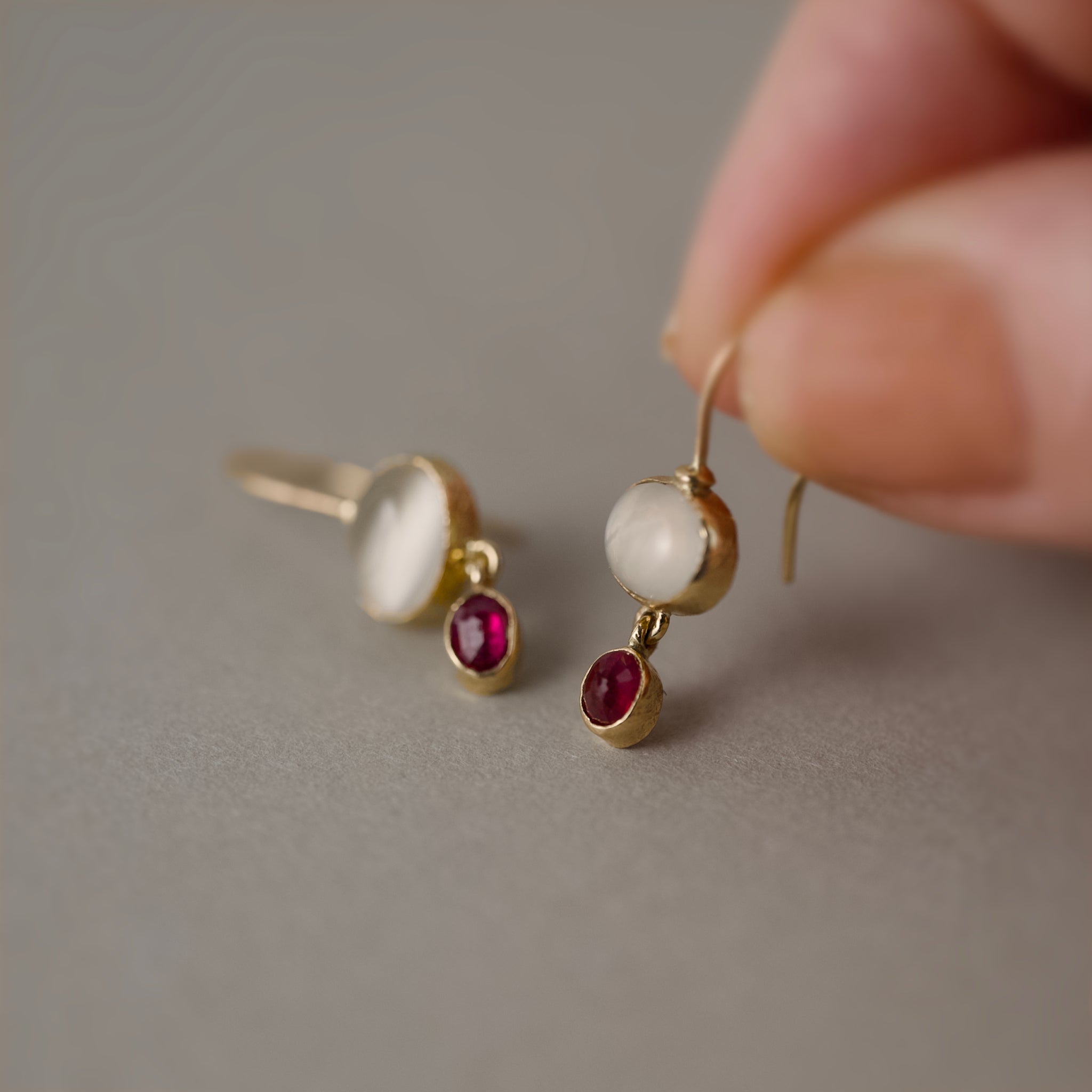 Gold earrings featuring moonstones and ruby gemstones held in hand
