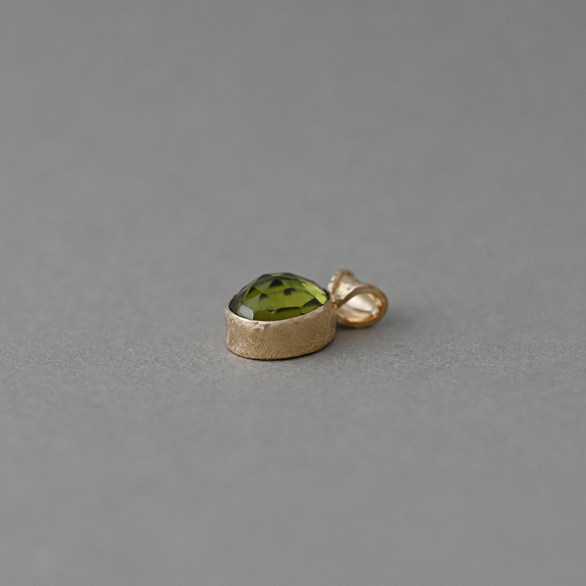 Side view of a 14ct solid gold Arizona peridot pendant showing the deep faceted gemstone and handcrafted bezel.