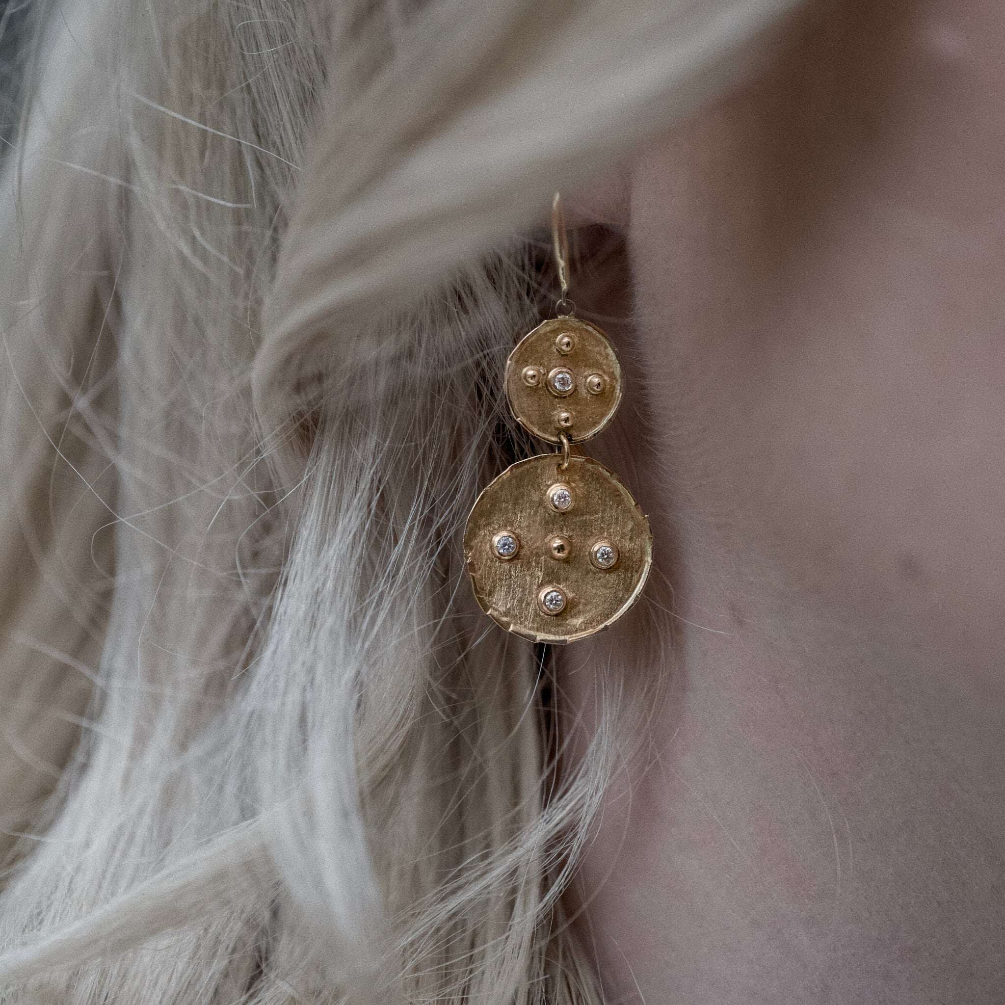 Close-up of Florin double disc diamond gold earrings worn on an ear with light blonde hair.