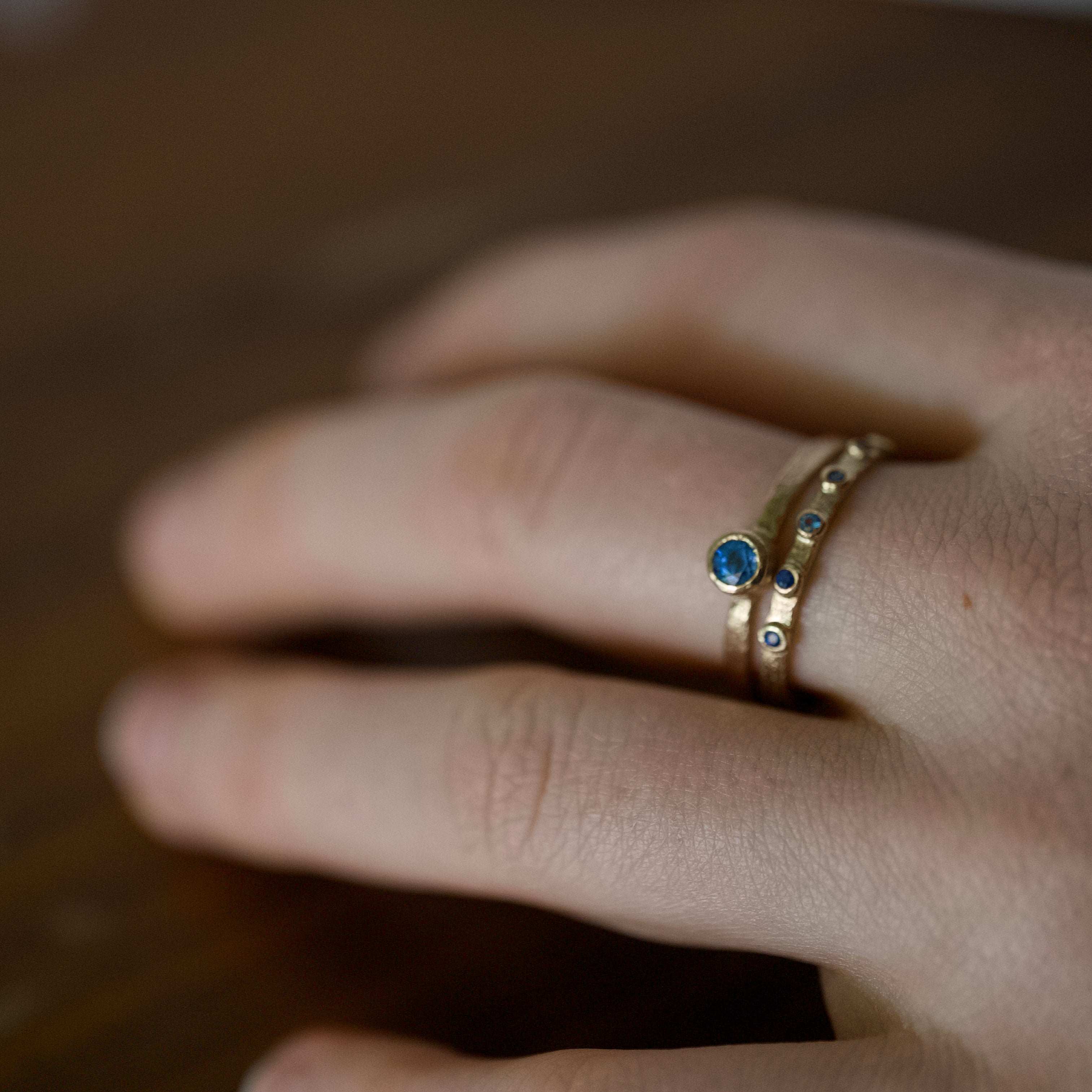 Soletta Sapphire Ring featuring a cornflower blue sapphire set in brushed gold on a finger