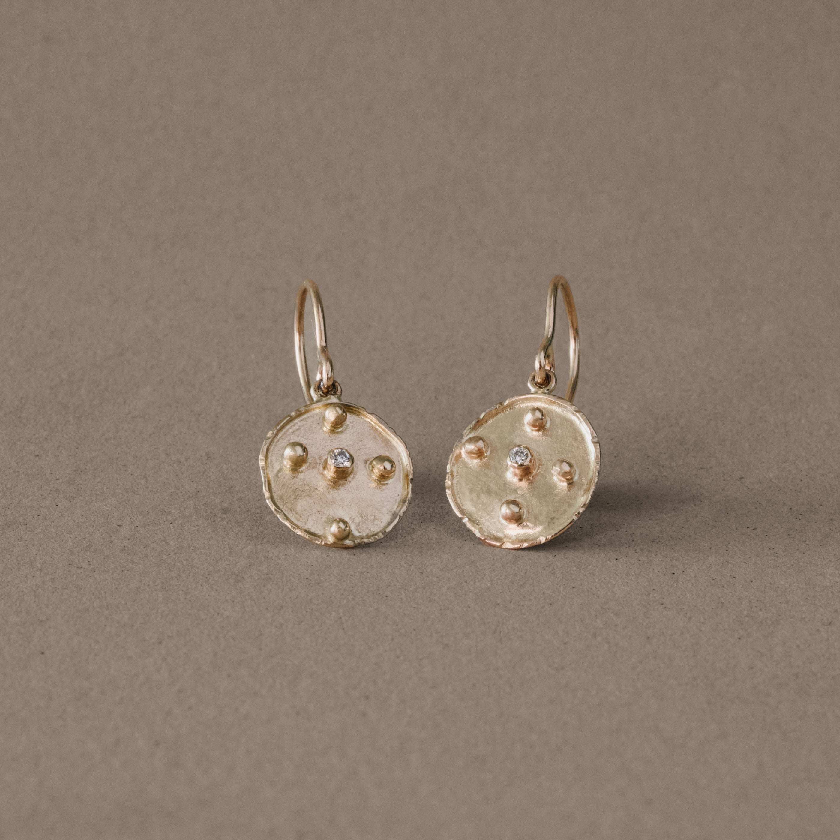 Gold disc diamond earrings on neutral background.