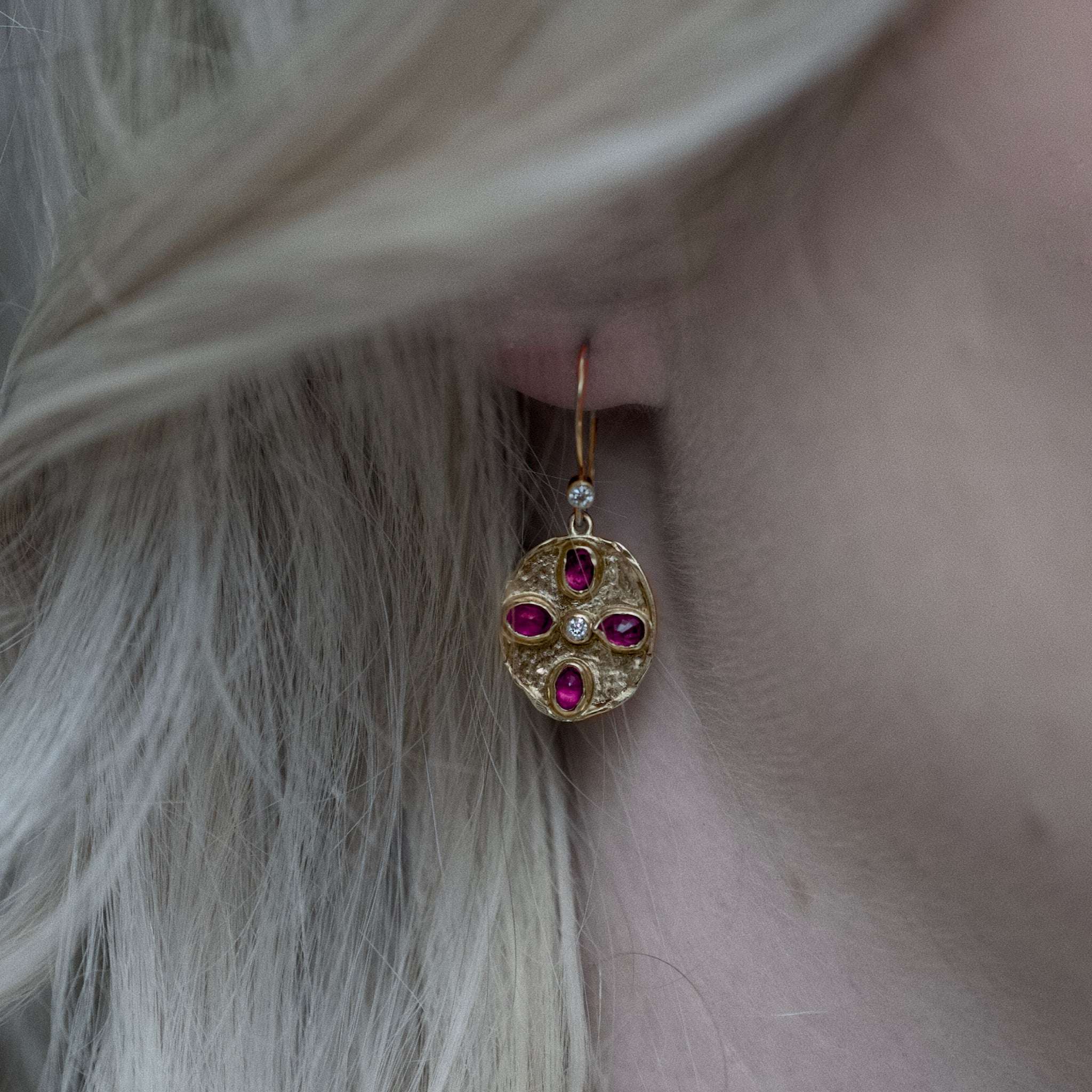 Close-up of gold Florin ruby diamond earrings with four oval rubies and diamonds worn on a blonde person's ear