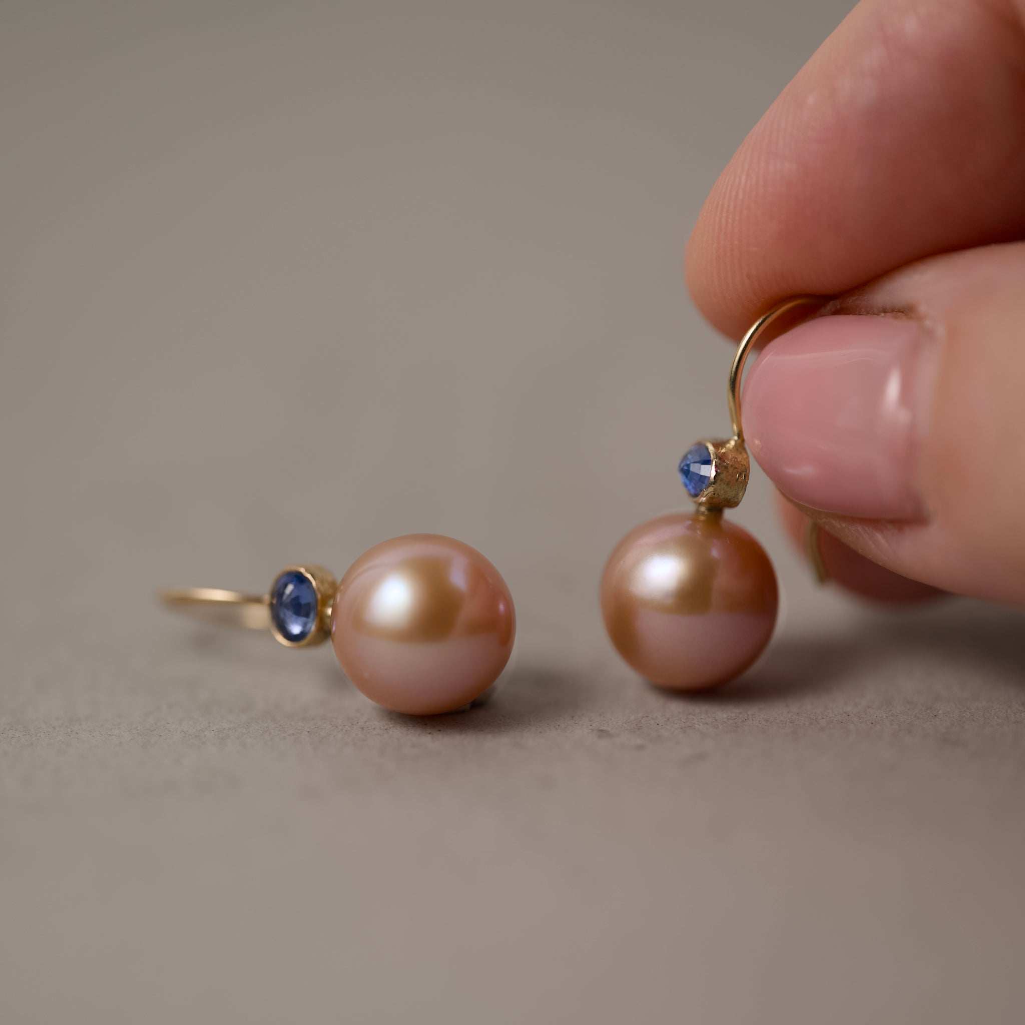 latte pearl earrings with oval sapphires held in fingers