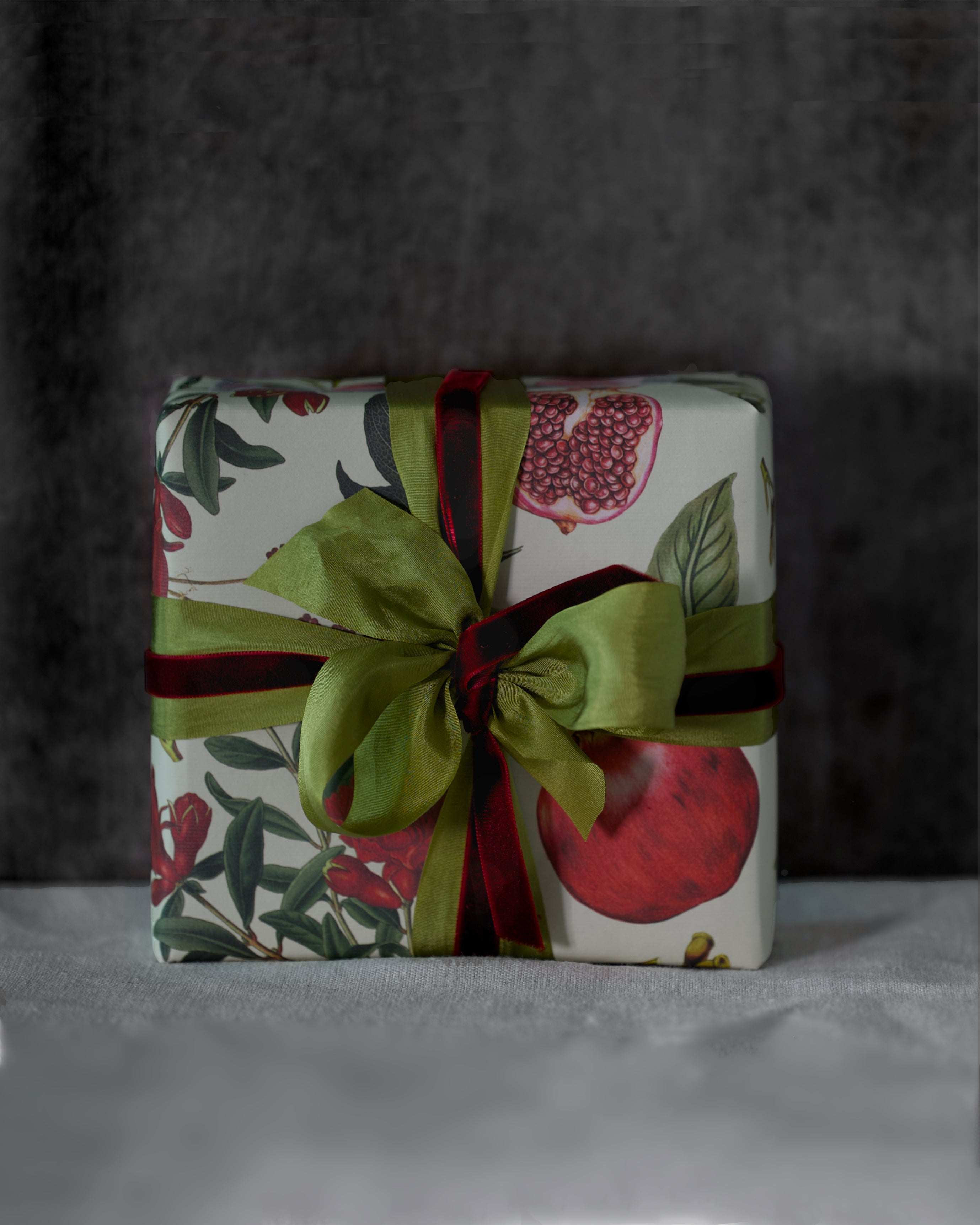 Elegant double sided gift wrapping with botanical pomegranate design, textured archive paper, and vermilion velvet ribbon bow