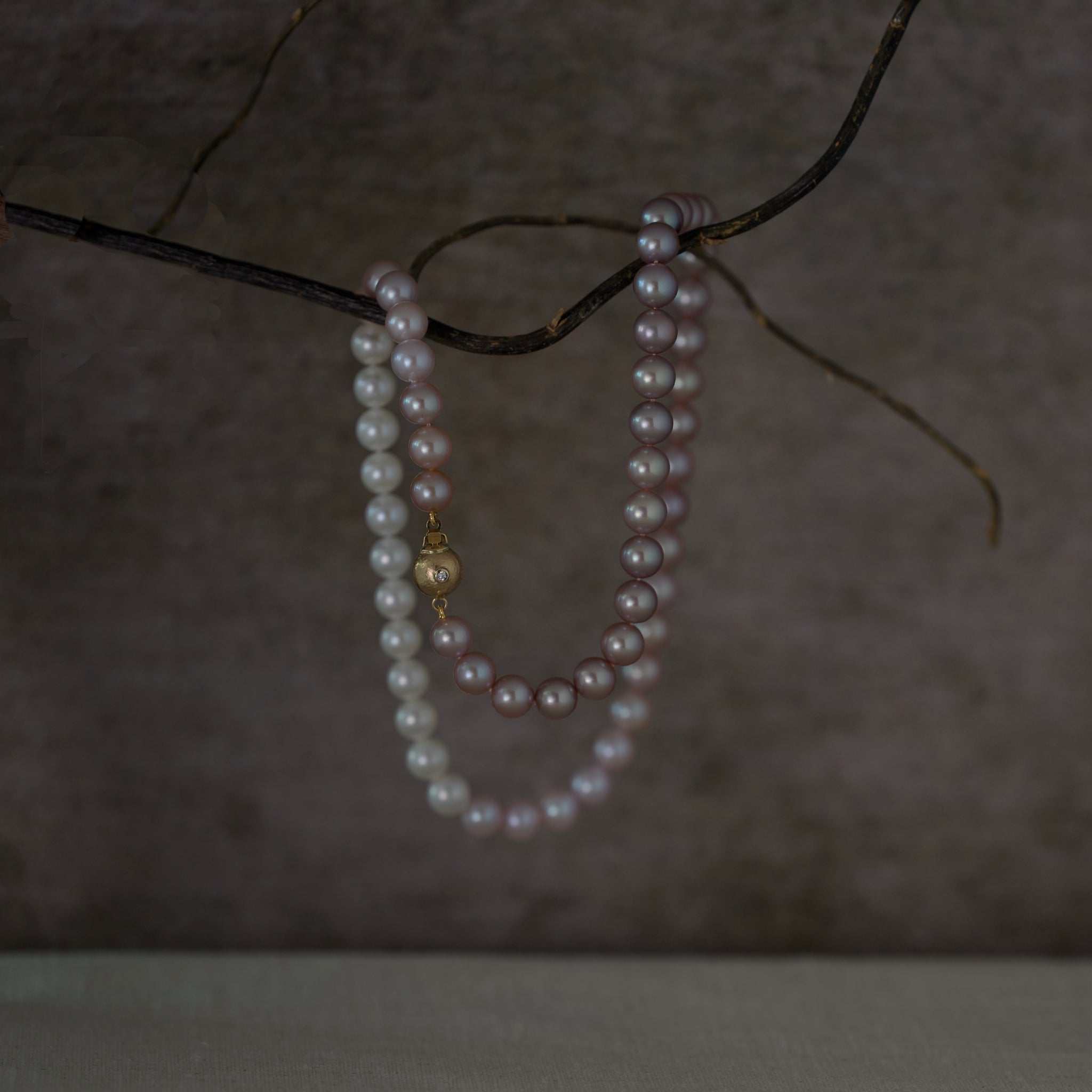 Colour-fade pink pearl necklace with lavender hues and gold clasp adorned with ruby and diamond.