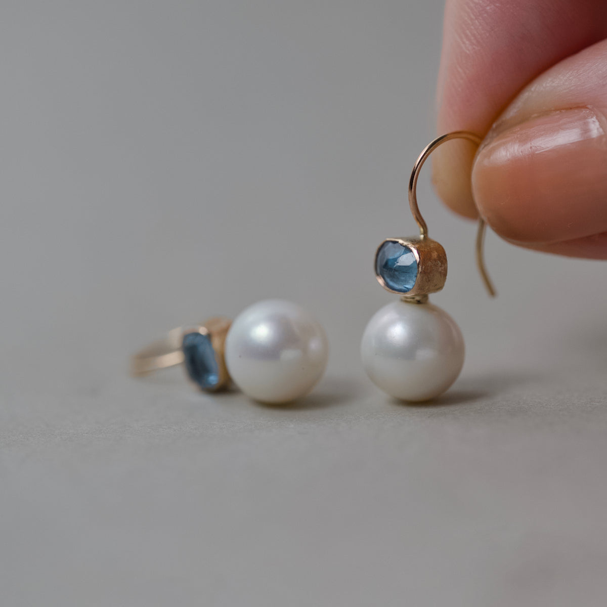 Aquamarine pearl earrings with gold accents showcasing icy blue aquamarine and milky pearls held in fingers.