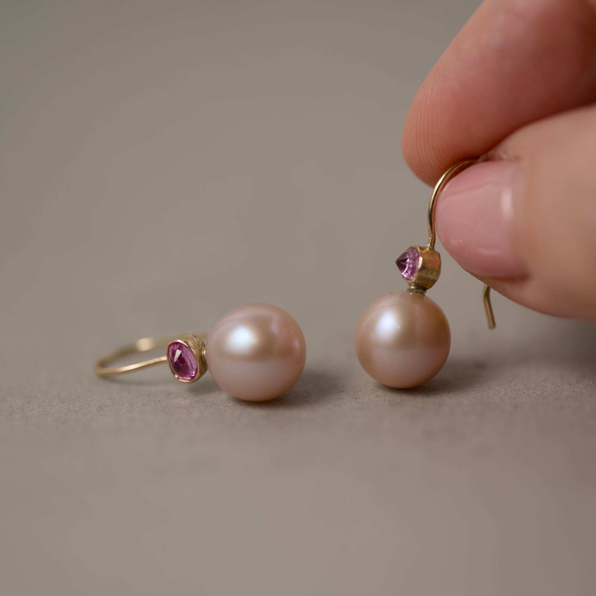 Pink Pearl Earrings with Rose Sapphires in 14ct Gold held by a hand