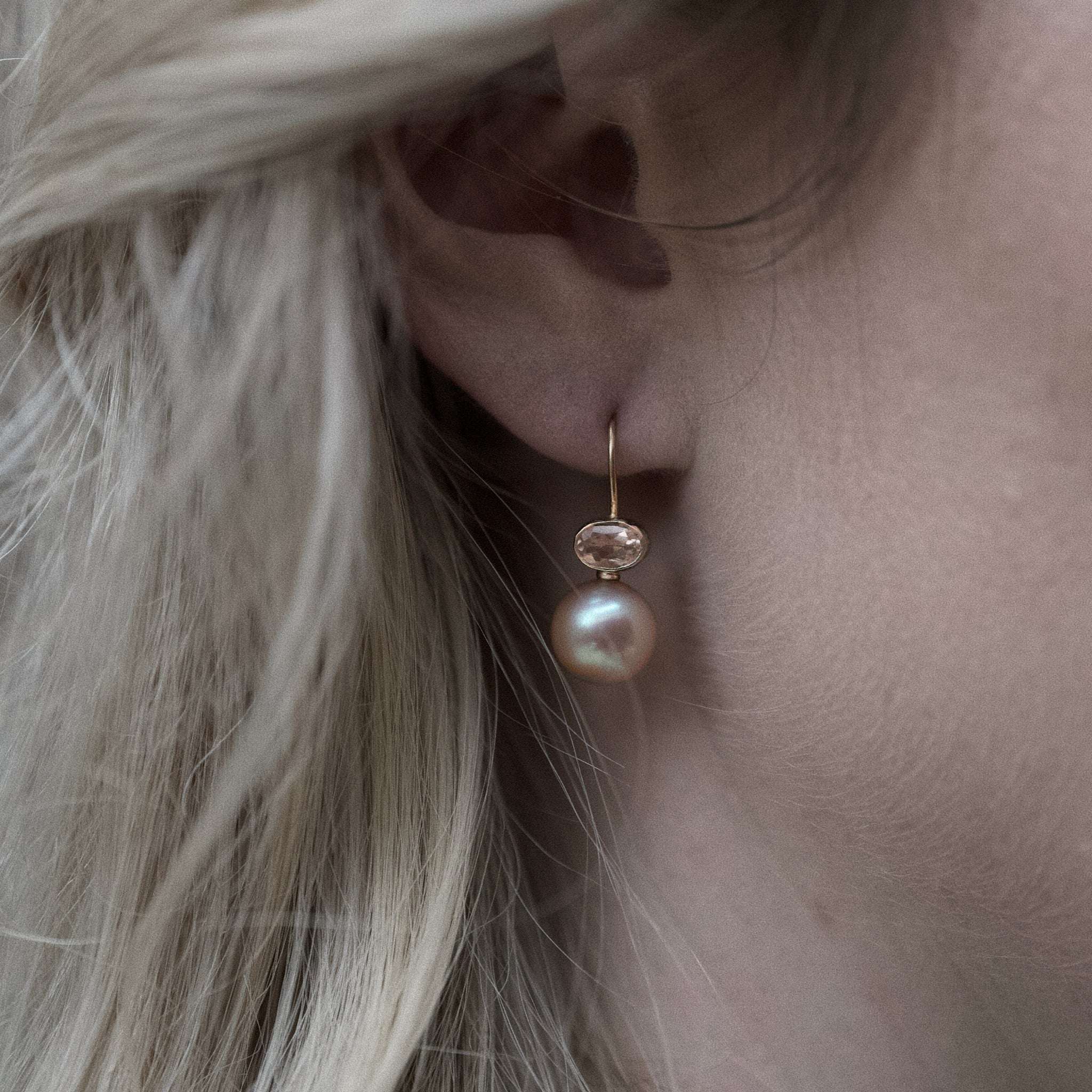 Close-up of an ear wearing delicate Morganite pink pearl earrings with gold setting