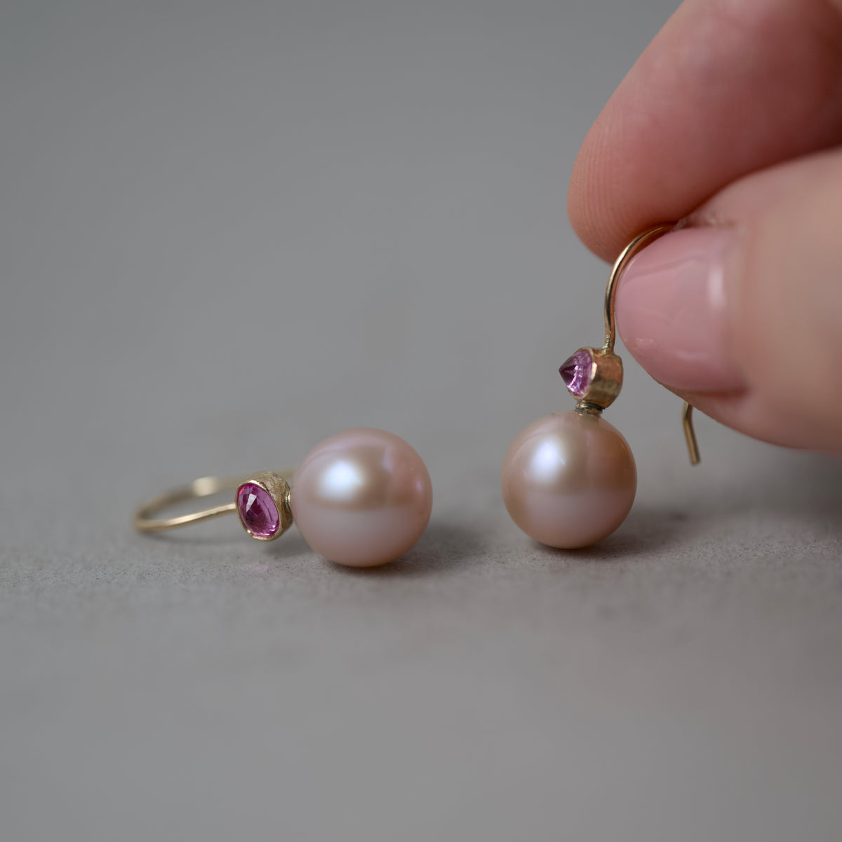 pink sapphire and Edison pearl earrings in 14ct gold hold in fingers