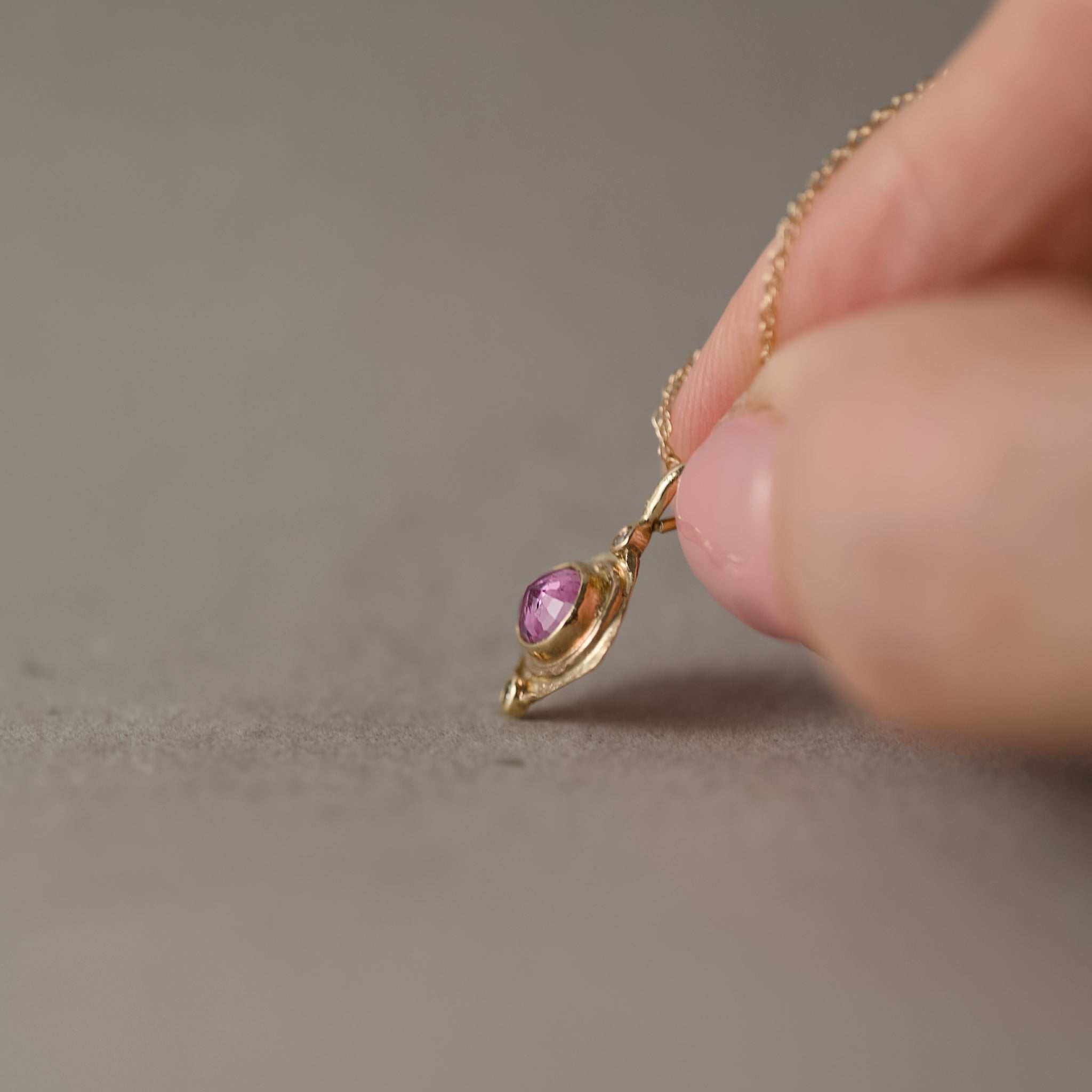 pink sapphire diamond pendant with chain held in fingers
