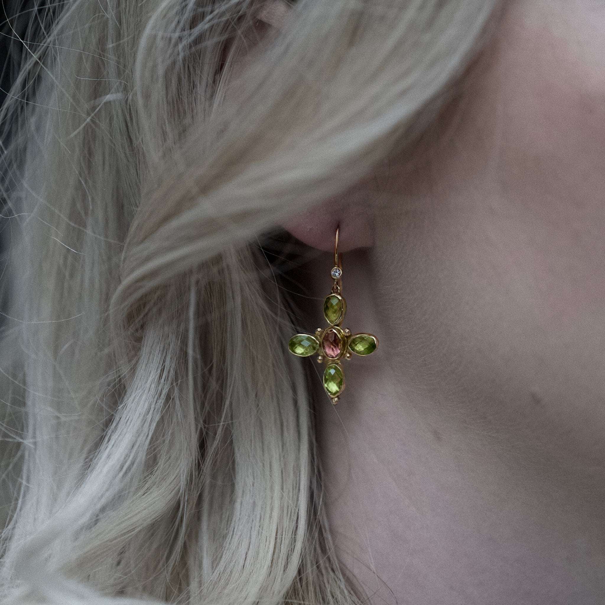 Close-up of a woman's ear wearing gold Quattro Peridot Tourmaline Diamond earrings with green peridot and pink tourmaline stones