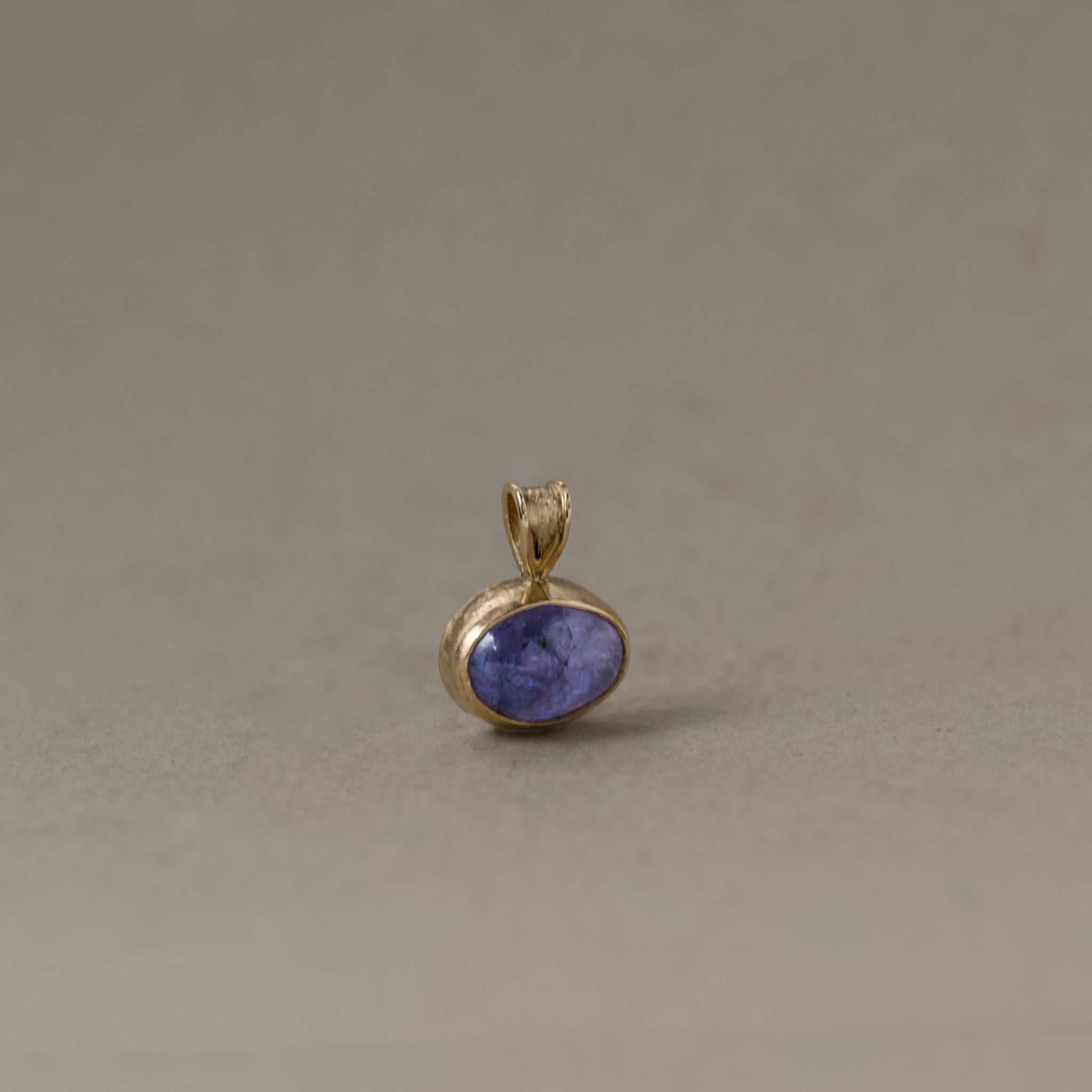 Close-up of Uno Tanzanite pendant necklace with violet hues set in gold, symbolizing tranquility and spirit