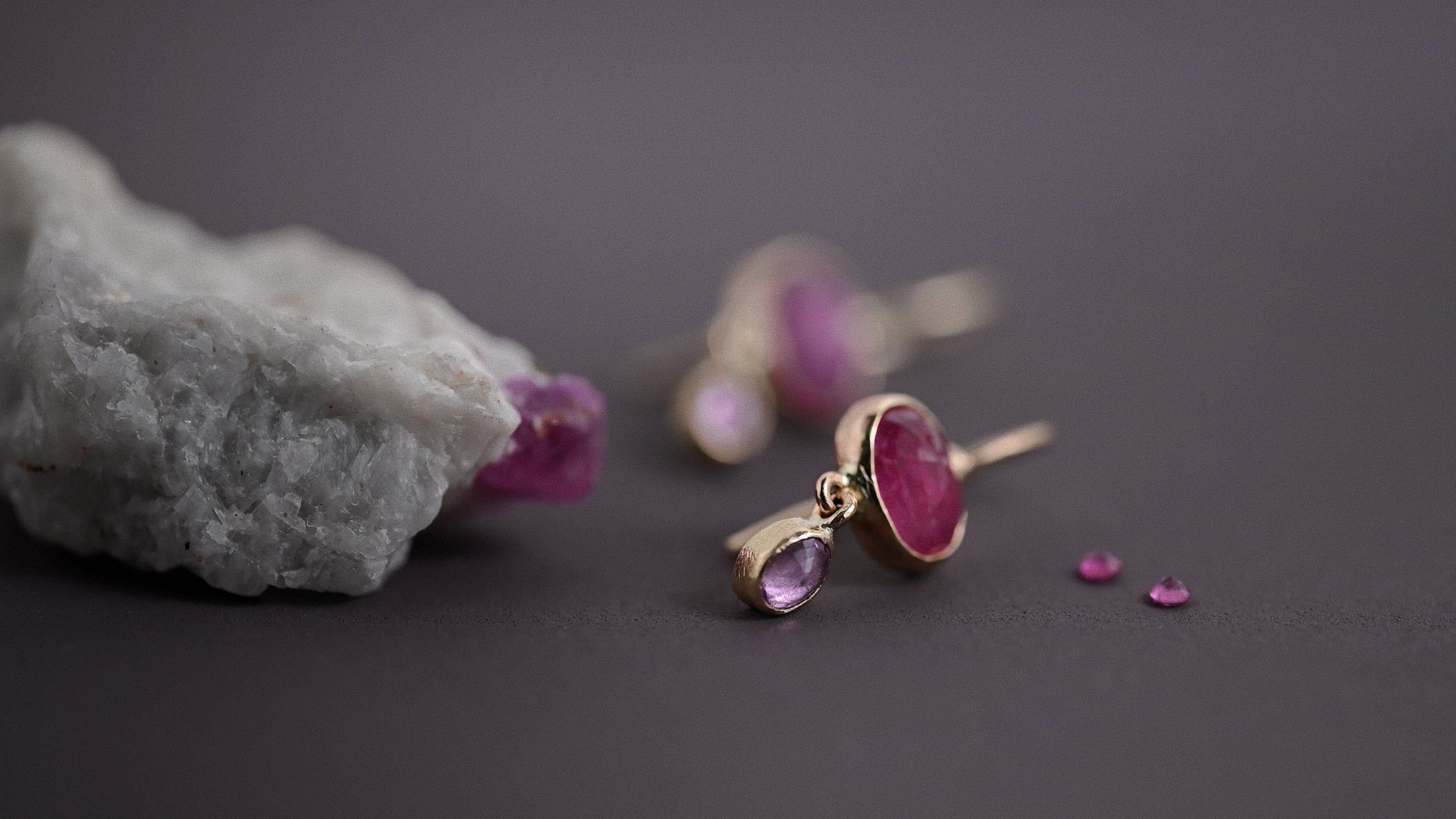 14ct solid gold ruby and pink sapphire earrings beside a rough ruby crystal.