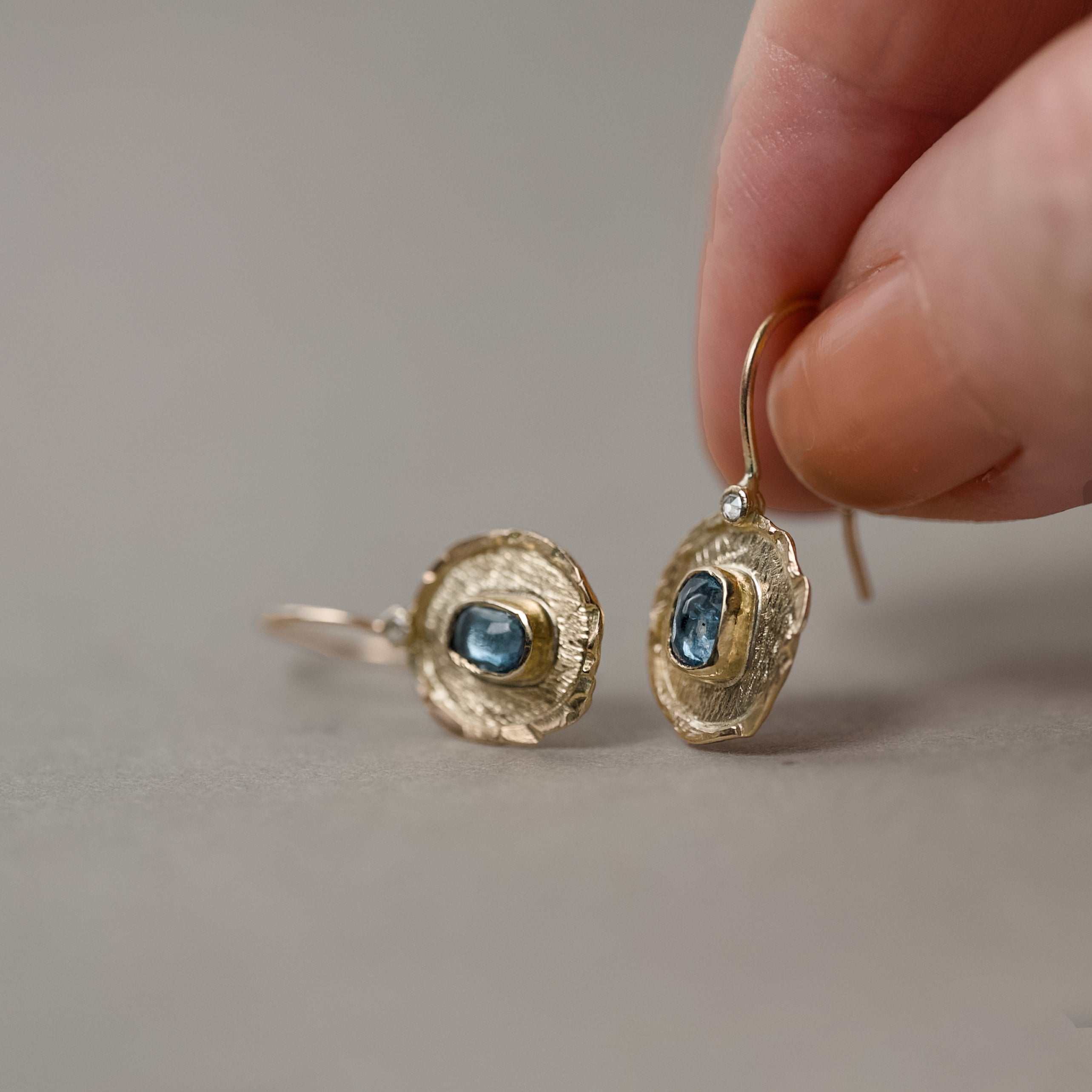 Florin aquamarine 14ct gold earrings held in fingers 