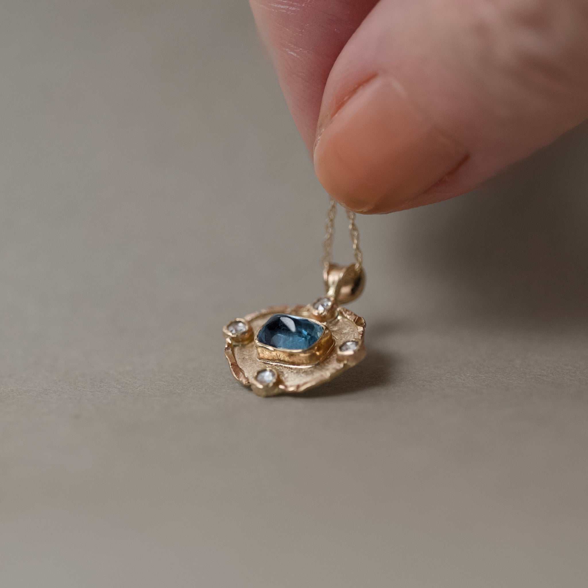 Florin aquamarine diamond pendant with 14ct gold chain held in fingers 