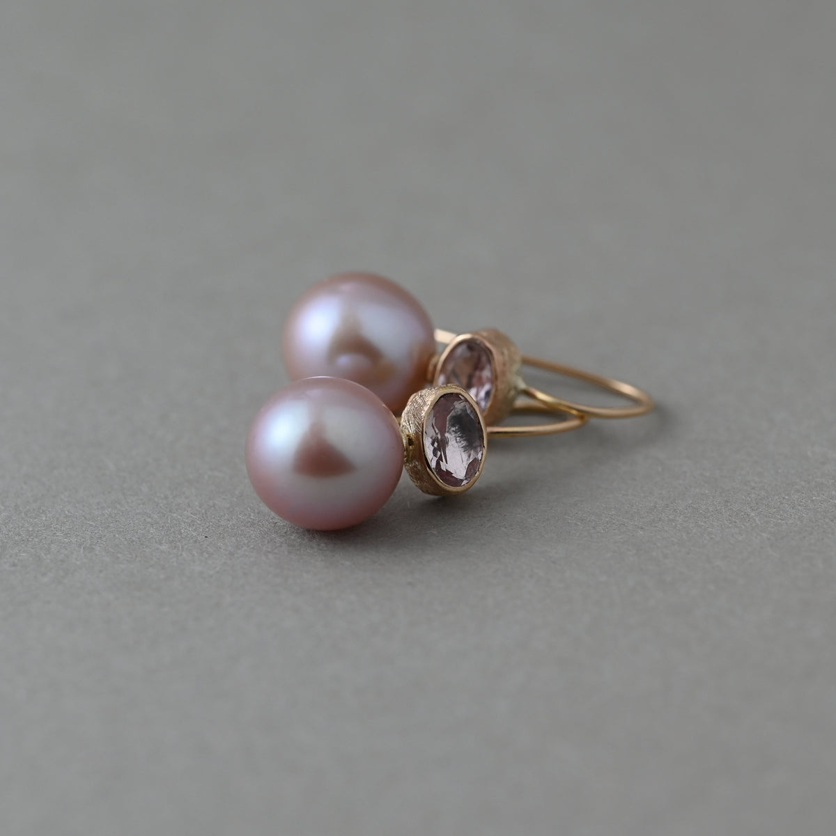 Morganite and pink freshwater pearl earrings in 14ct solid gold, laid on their side showing the gemstone settings and pearl profile