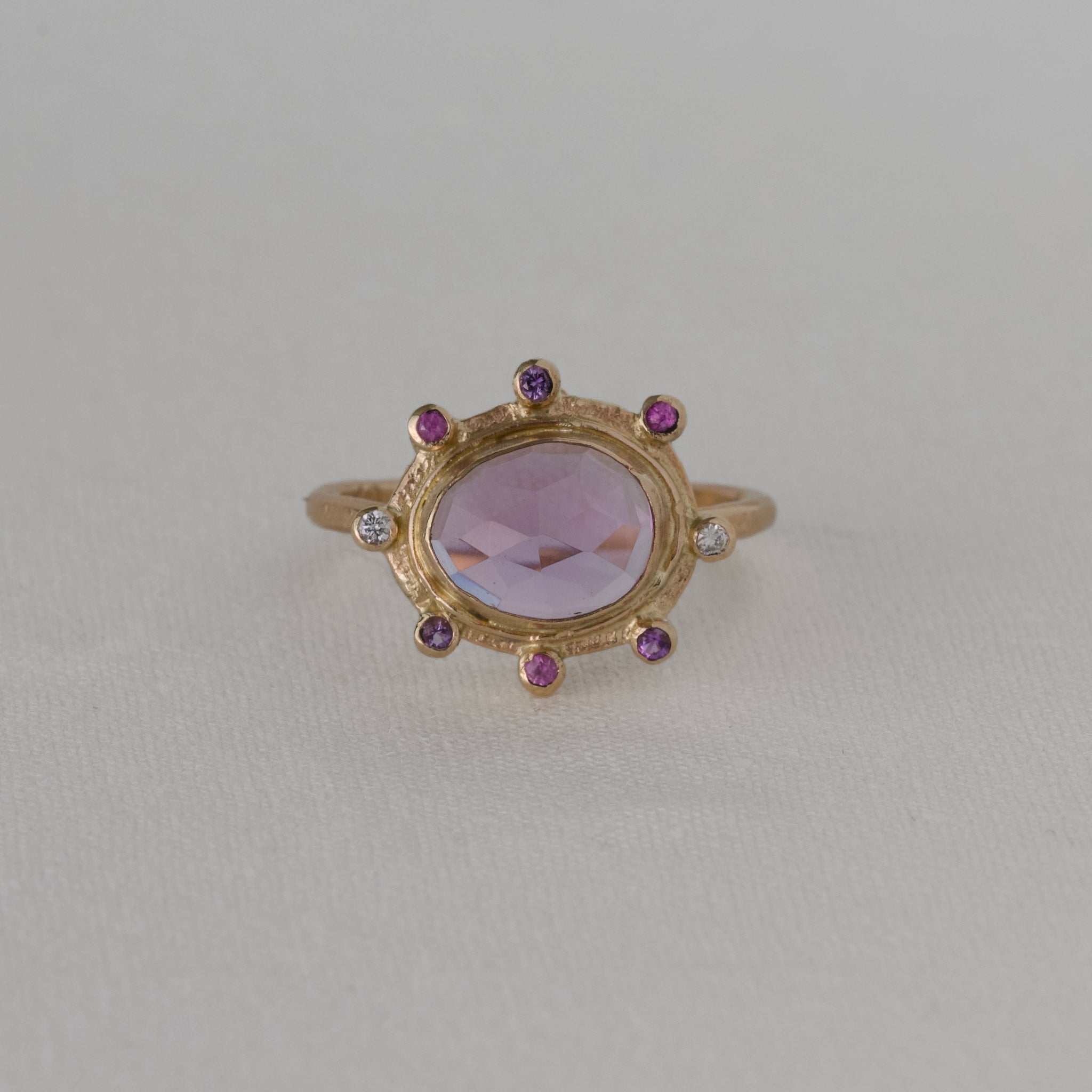 Amethyst ring with lilac gemstone set in gold, adorned with sapphires and diamonds.