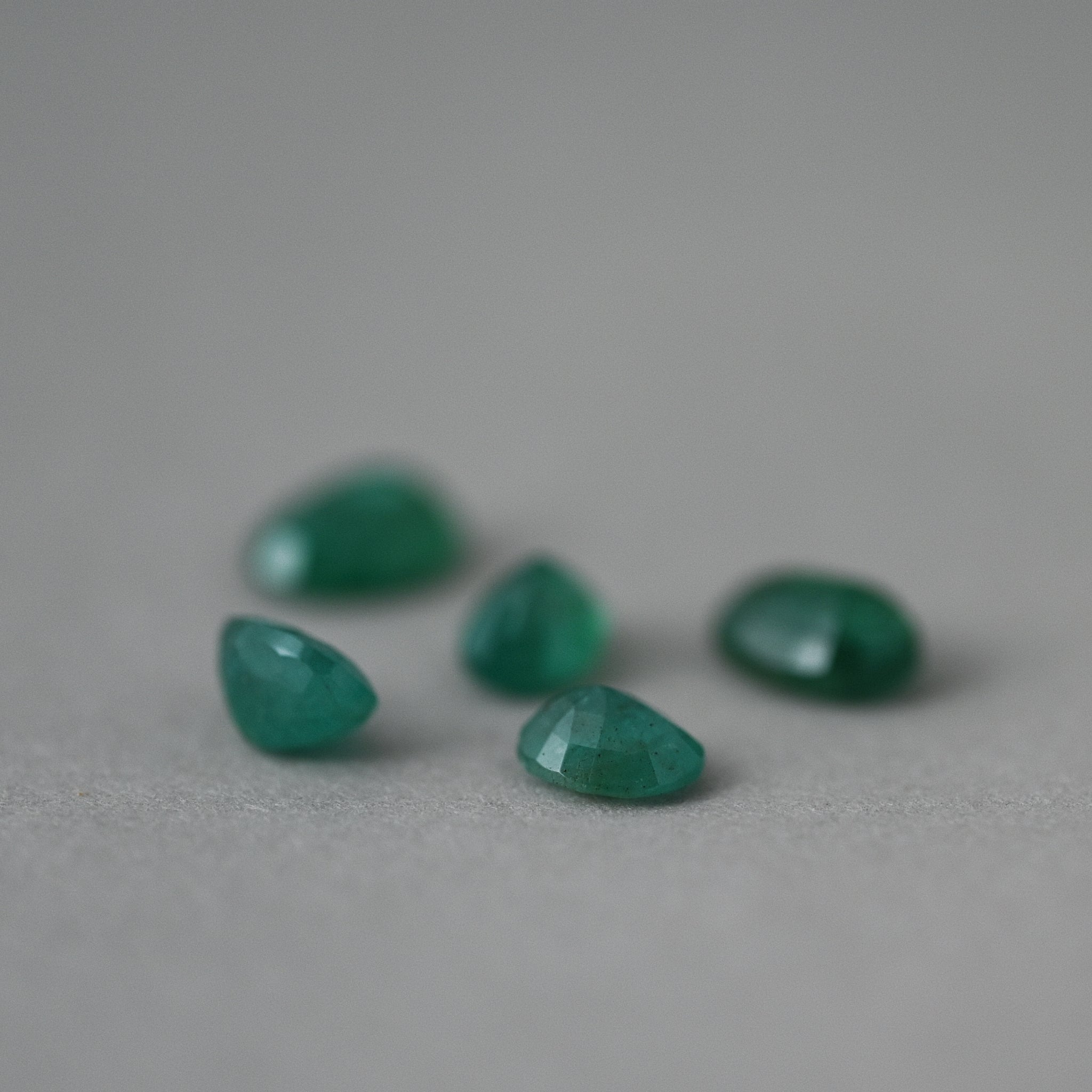 loose Zambia emerald gemstones on grey paper