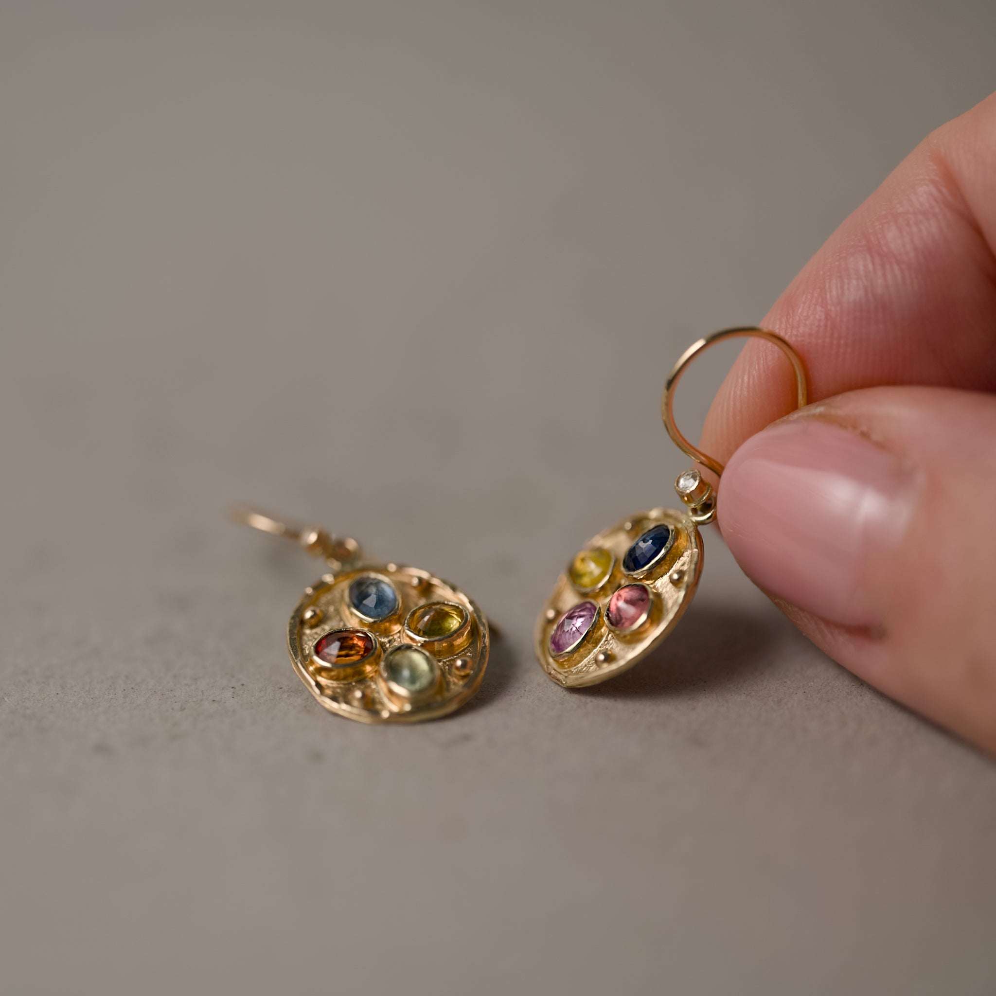 Florin confetti sapphire diamond earrings held by fingers