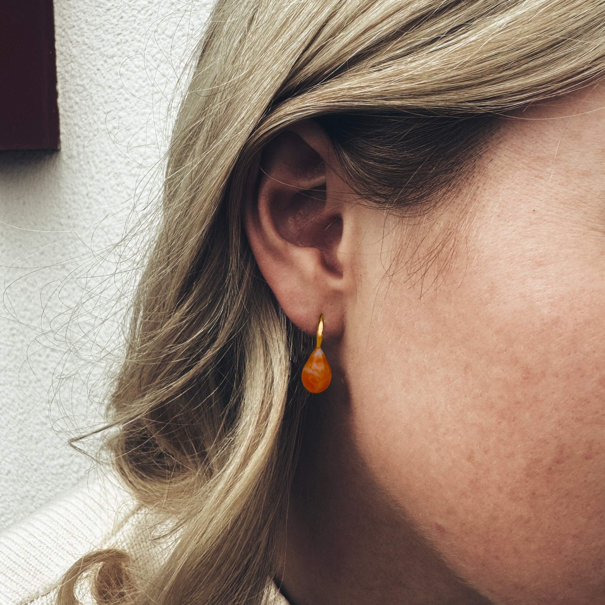 Bella Mandarin Murano Gold Drop Earrings in orange glass with gold settings worn by a person.