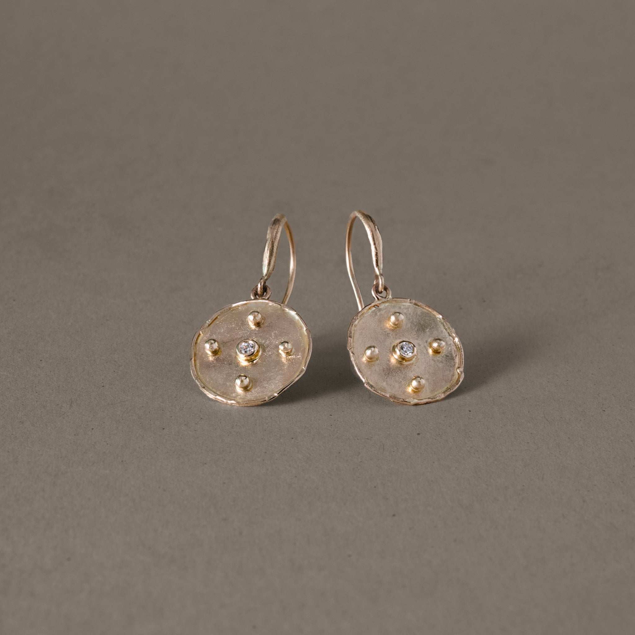 Gold disc diamond earrings with pure diamonds on a gray background.