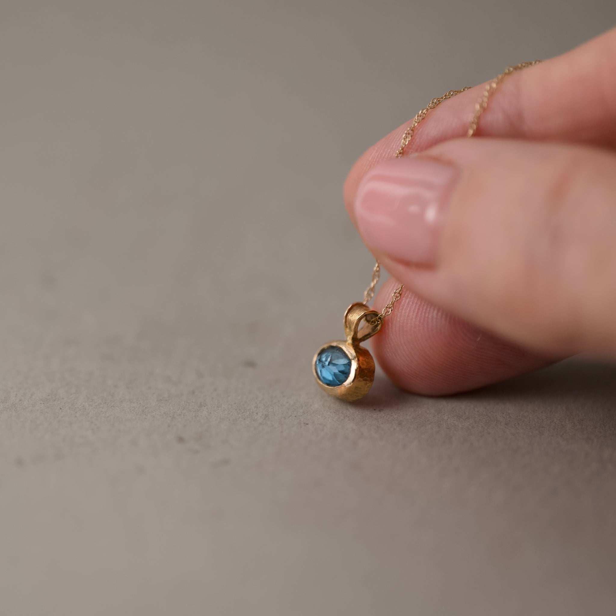 London blue topaz pendant and chain held with fingers 