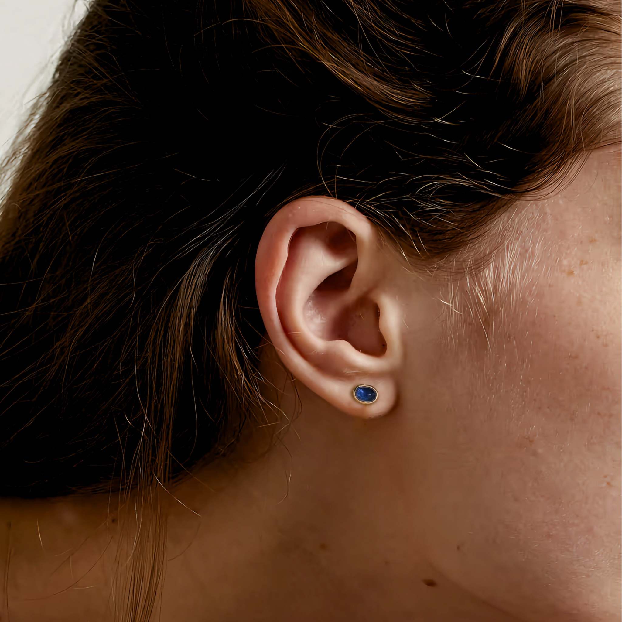 Sapphire earrings worn by a person, featuring deep blue sapphires set in gold.