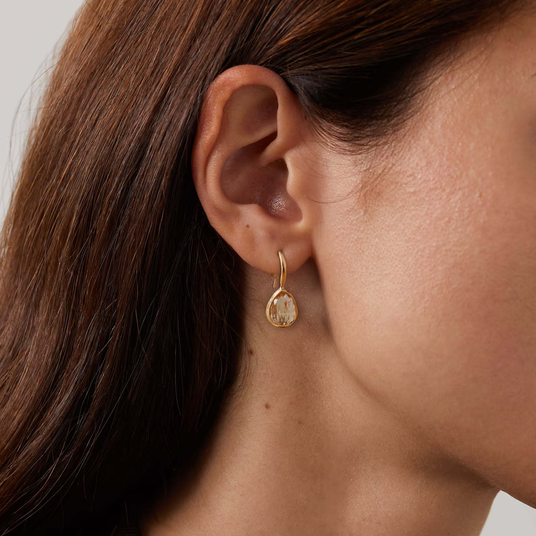 Handcrafted Topaz Earrings in gold on model's ear.