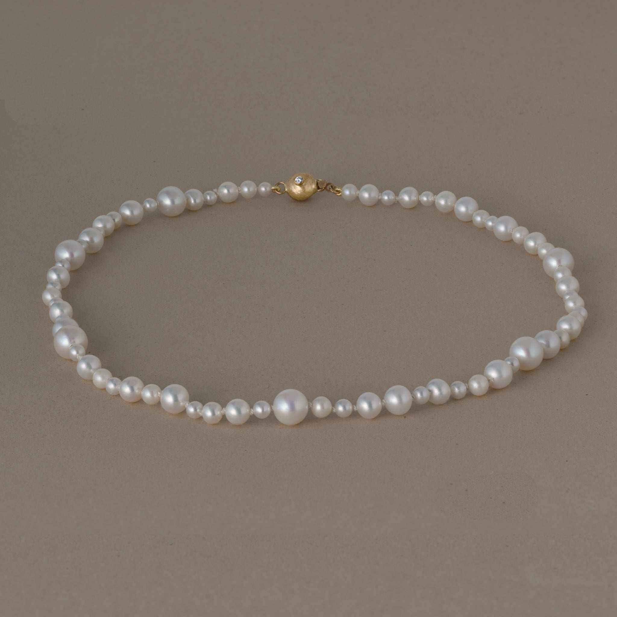 Ondina Freshwater Pearl Necklace with graduated white pearls and gold clasp on neutral background