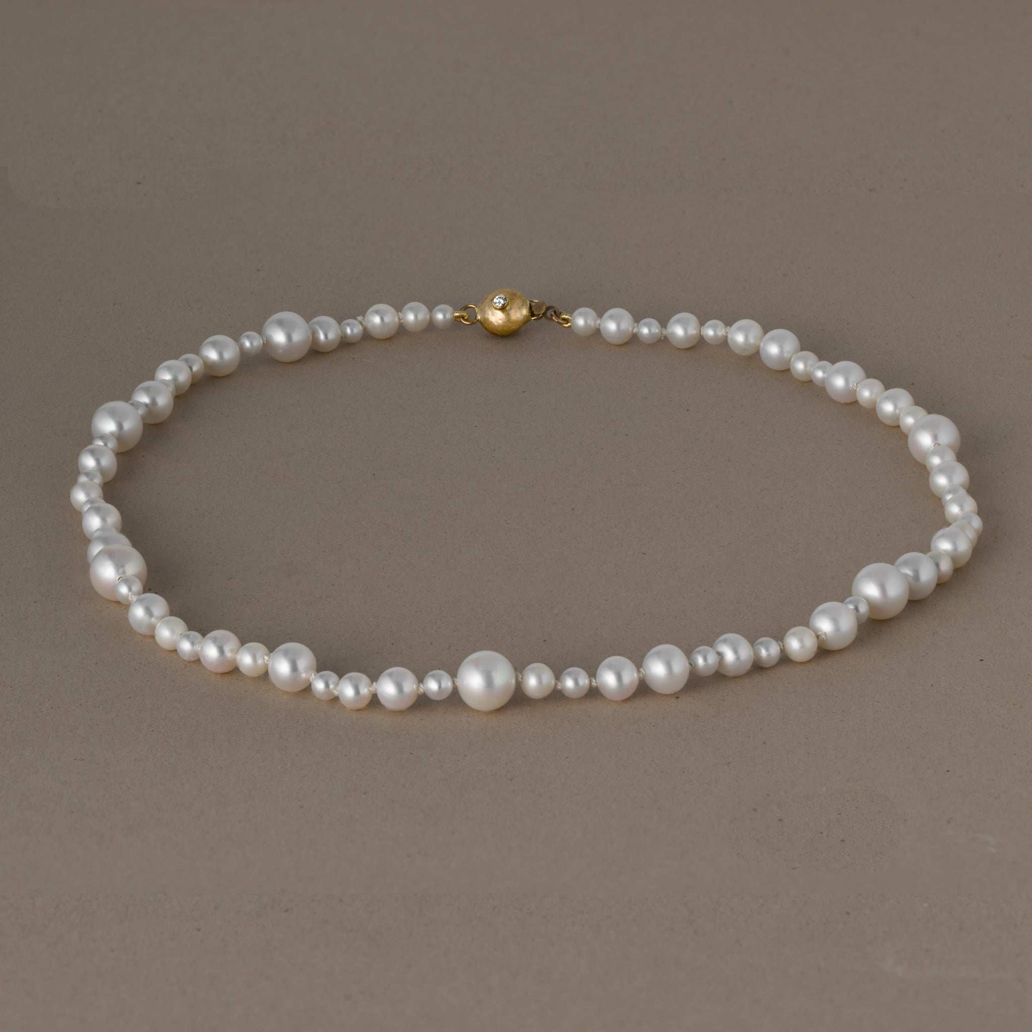 Ondina Freshwater Pearl Necklace with varying pearl sizes and gold clasp on neutral background