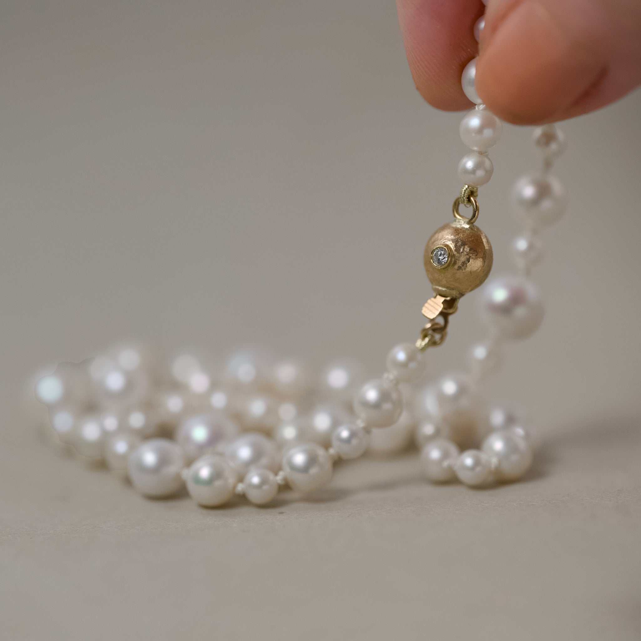 ondina pearl necklace strung on silk with 14ct gold ball clasp held in fingers