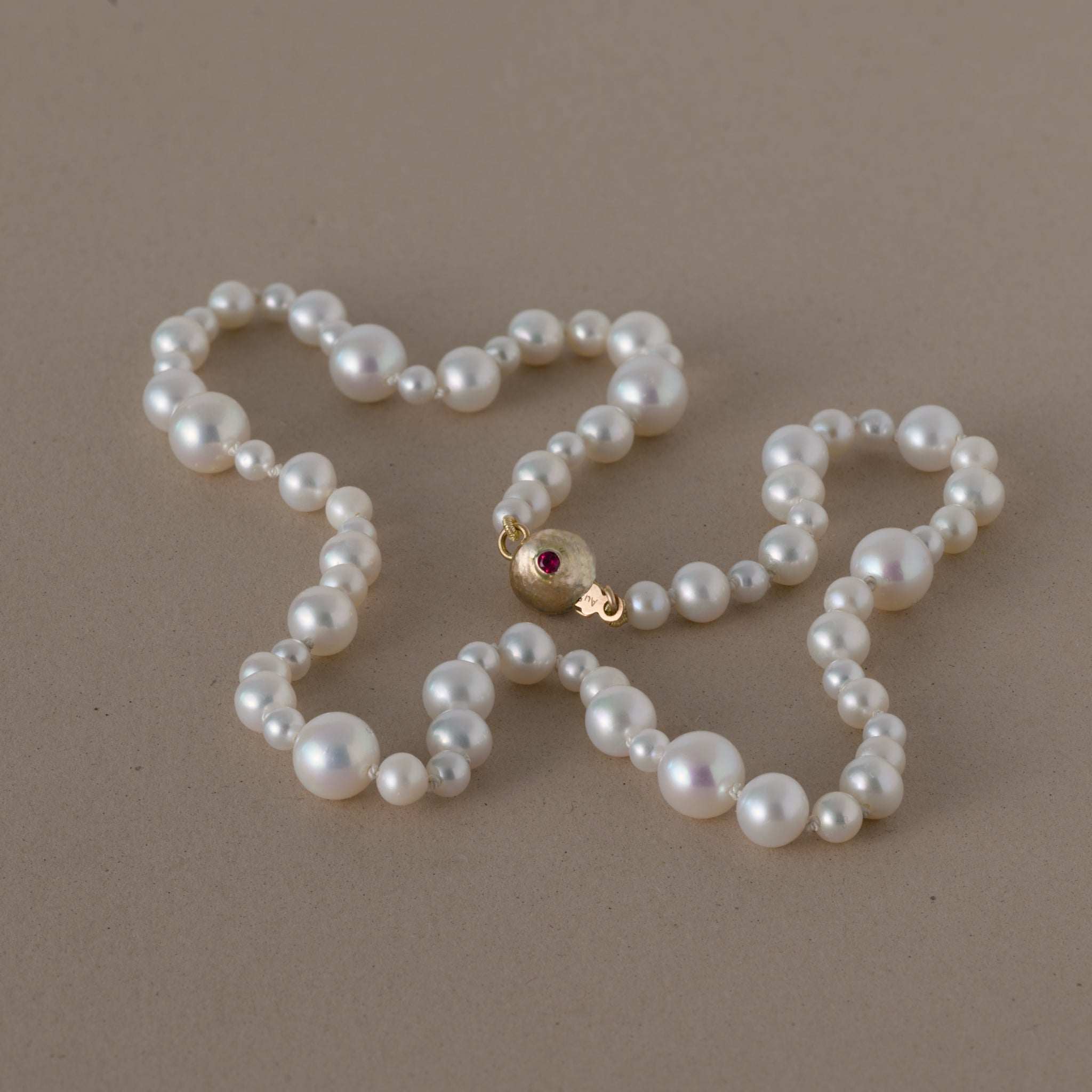 Ondina Freshwater Pearl Necklace with round pearls and gold clasp set with ruby on beige background