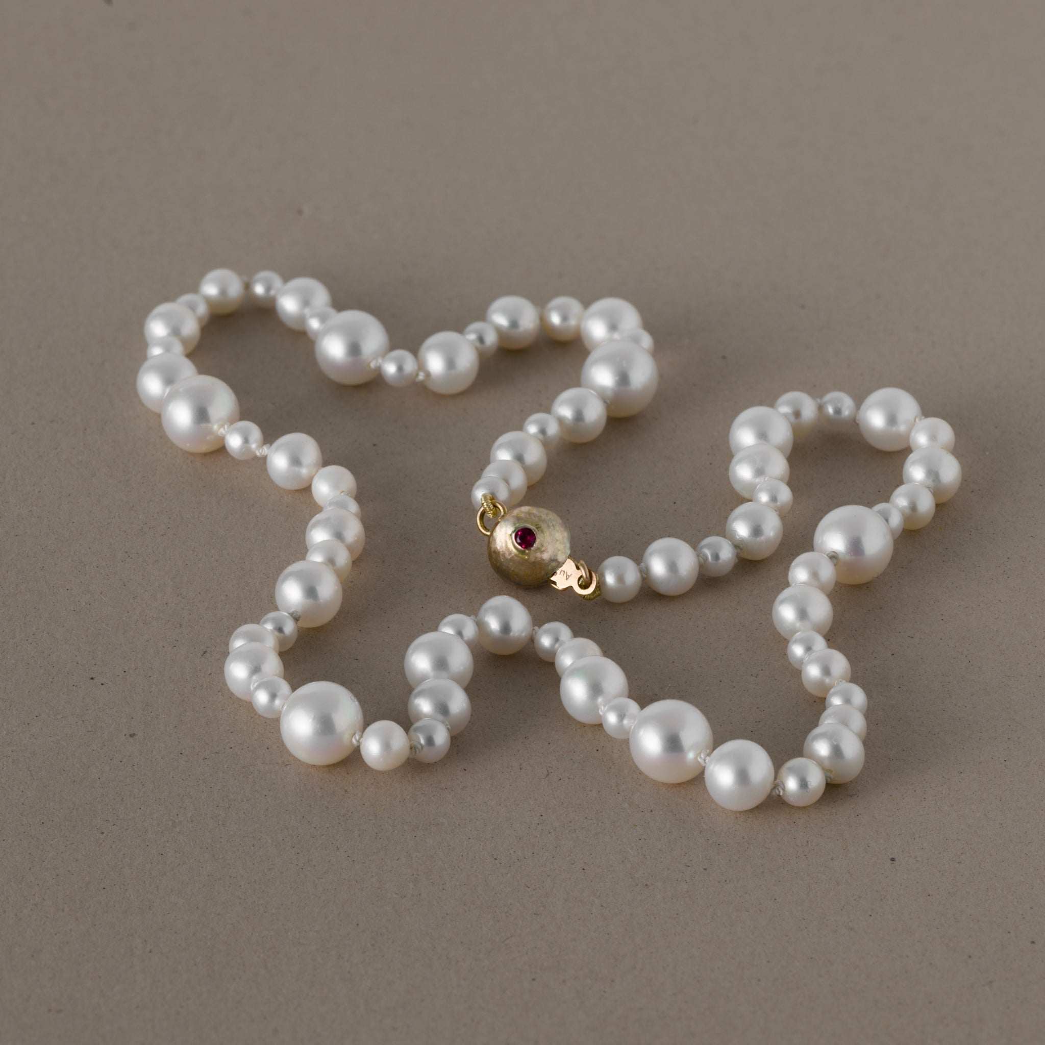 Ondina freshwater pearl necklace with round white pearls and a gold clasp featuring a ruby gemstone