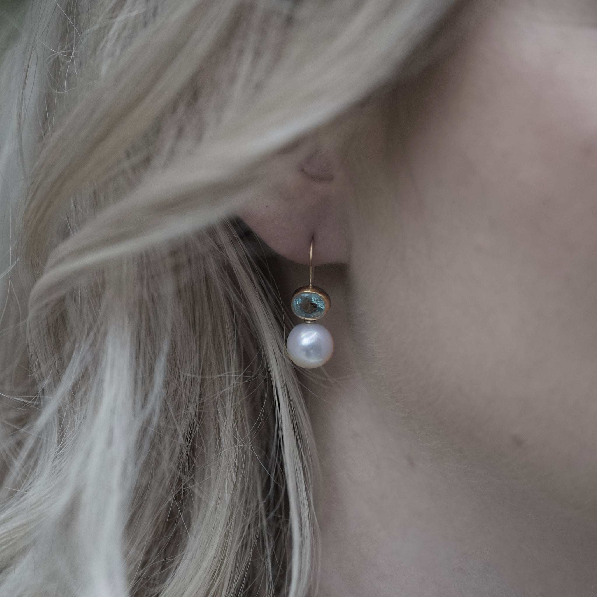 Close-up of Paraíba tourmaline and freshwater pearl earrings set in 14ct gold worn on ear