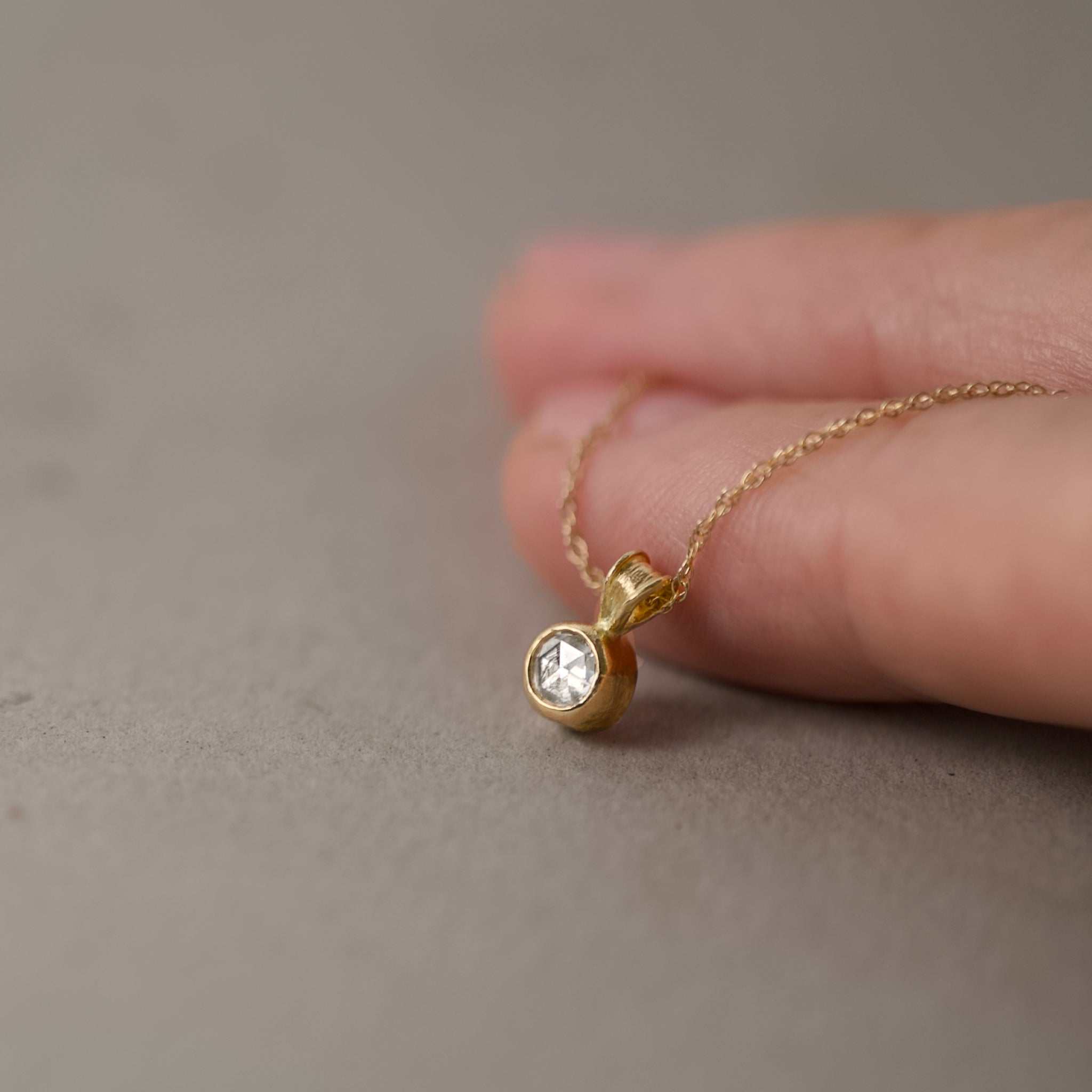rose cut diamond pendant on chain held by fingers 