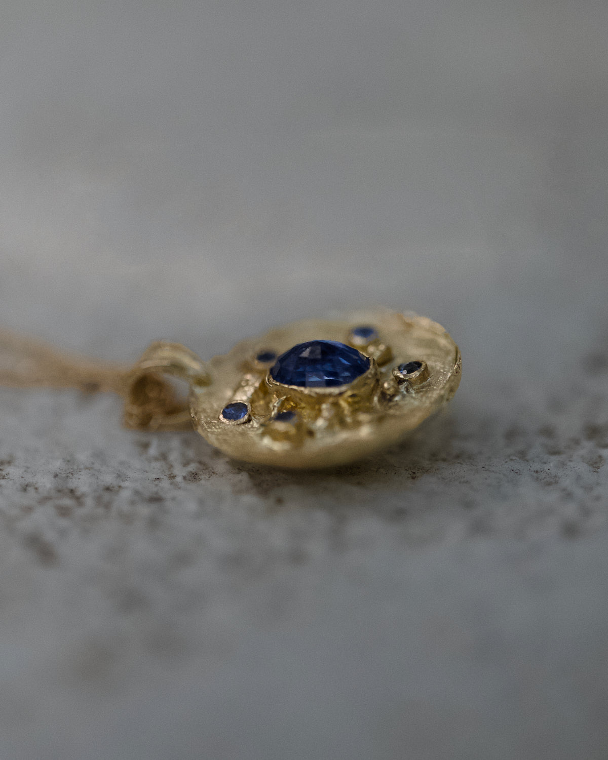 Ceylon sapphire Florin medallion in solid 14ct gold, photographed from a low angle on a textured grey surface