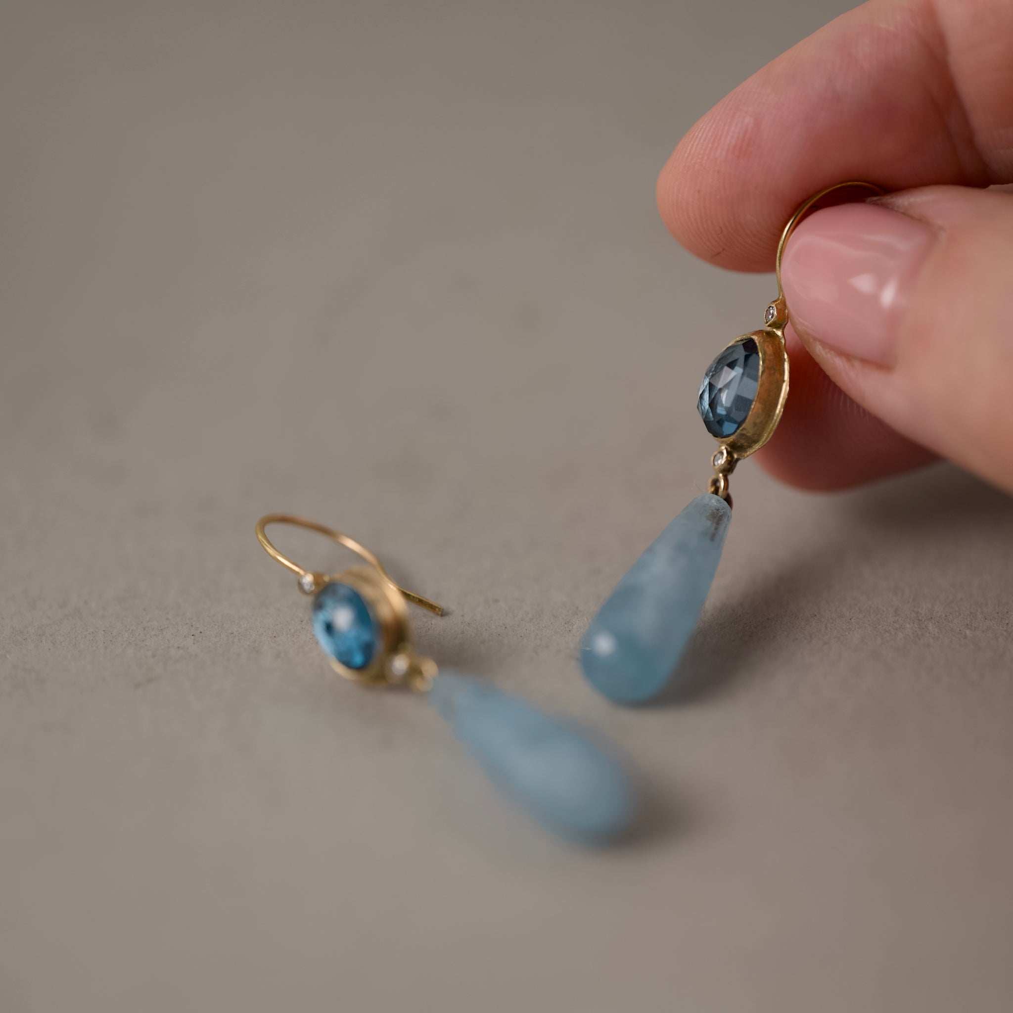 sera London blue topaz aquamarine drop earrings held in fingers 
